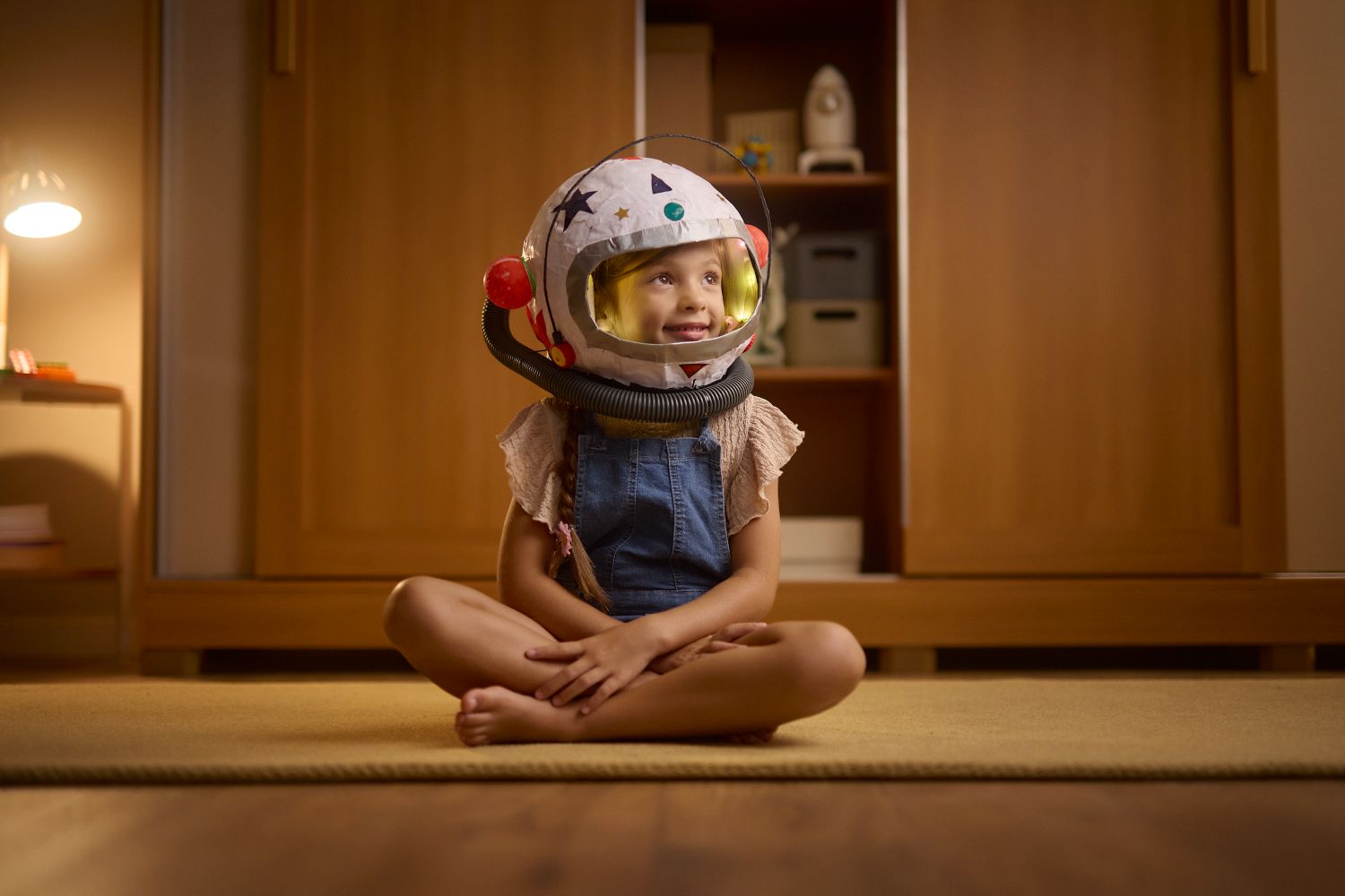 Criança fantasiada de astronauta sorrindo sentada no quarto.